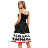A woman with long hair is wearing a sleeveless black top and a knee-length black skirt. The skirt, described as a "skirt women's ladies Christmas print knee-length skirt stretch high waist wild Christmas party sexy skirt," has a white border at the bottom featuring a print of black trees and reindeer. She is smiling, facing slightly away from the camera to showcase the design of her festive attire.